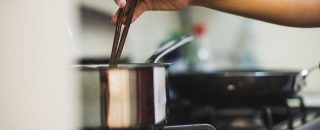 Young woman stirring pan on cooker top with chopsticks