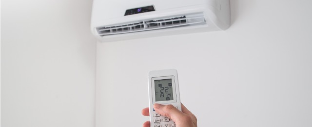 Hand holding remote control for air conditioner on white wall; 空調