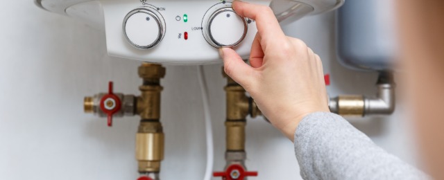 Female hand puts thermostat of electric water heater (boiler) in economy mode