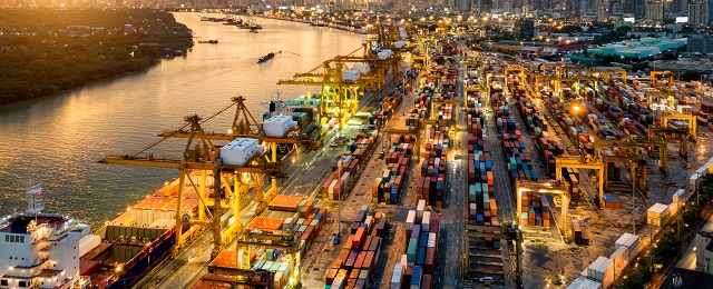 Aerial view of international port with Crane loading containers in import export business logistics with cityscape of modern city at sunset