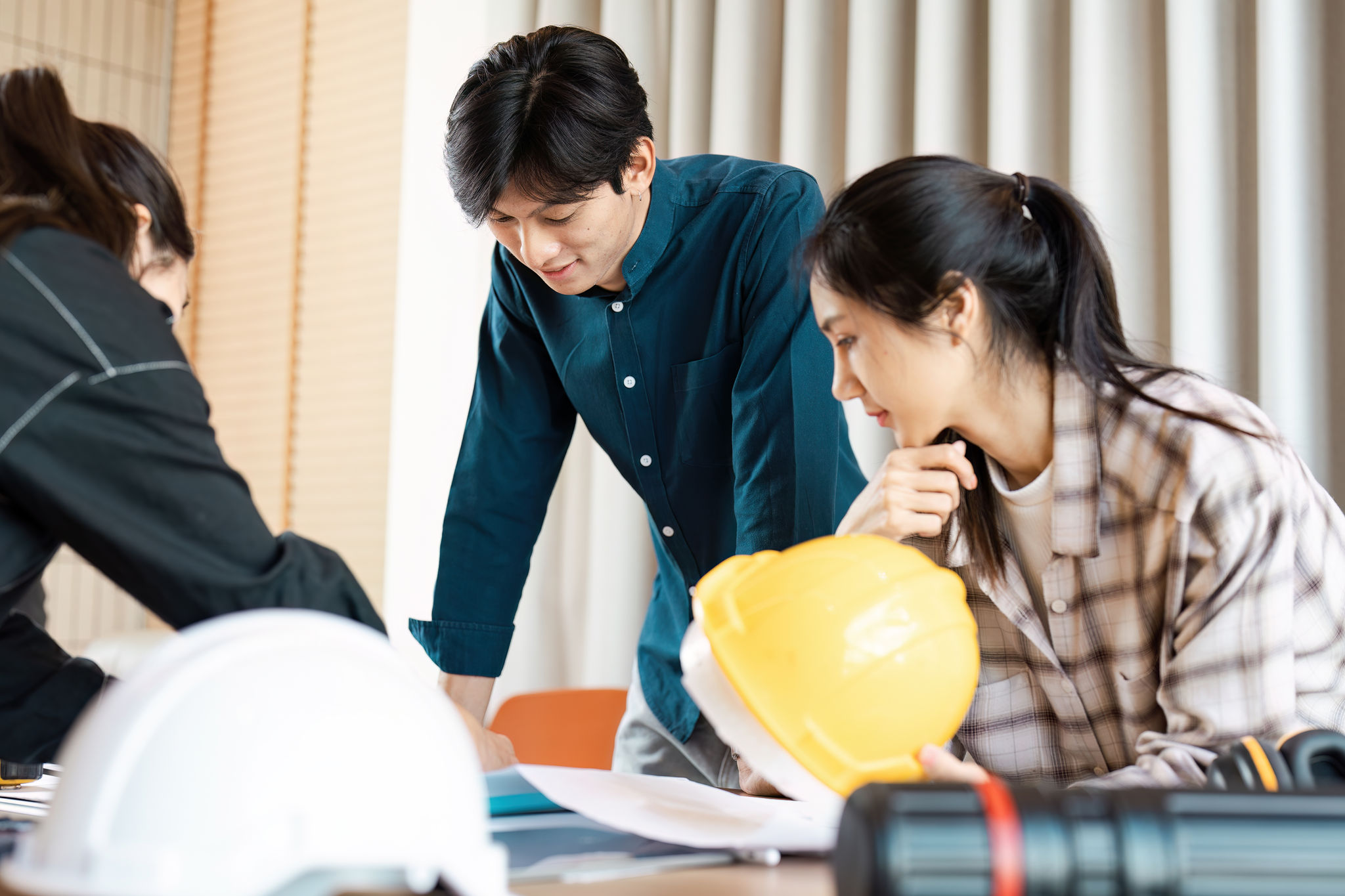 Group of young professionals discussing construction plans with blueprints and safety gear in a modern office setting